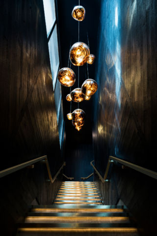 The globular almost molten sensation of Tom Dixon's Melt Pendant Copper lighting, set against the stained dark wood creates an atmospheric stairway in Alto