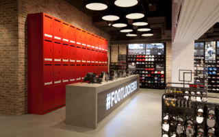A bank of brand red lockers, creates a strong signposting for the cash wrap area of the store, while the desk front features conveys changing brand messaging in Footlocker's Oxford St. store